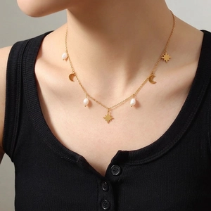 Gold necklace with star moon pendants and freshwater pearls shown on model neck