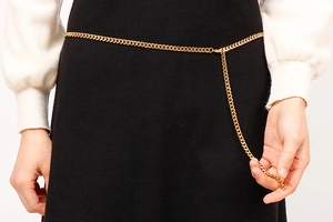 Close-up of stylish gold metal waist chain on white knit top and black skirt