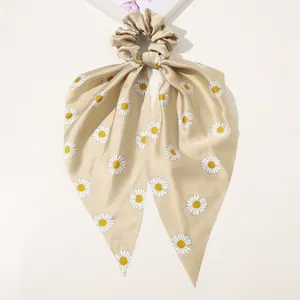 Close-up of champagne satin hair scrunchie with daisy prints and elegant long ribbons
