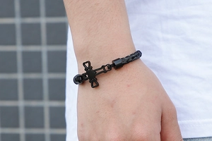 Close-up of men's black braided rope bracelet featuring a dark cross pendant on wrist