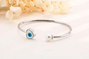 Detailed shot of silver heart evil eye bracelet with pearl on a beige surface