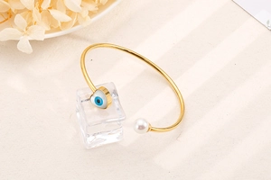Detail of gold open bracelet with heart evil eye charm and elegant white pearl decoration