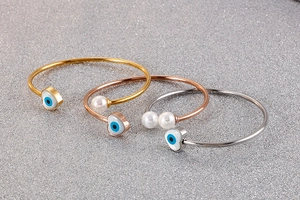 Three open bangles with evil eye heart charms and pearls in gold, rose gold and silver