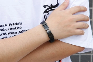 Close-up of men's black braided leather bracelet featuring a crystal-studded X-shaped metal clasp