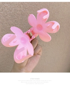 Detail of pink matte flower hair claw clip with metal spring mechanism held by hand