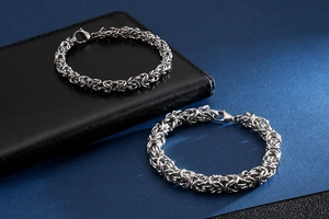 Detail of silver Byzantine weave titanium steel bracelets with lobster clasps on dark surface