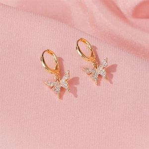Détail de boucles d'oreilles huggies dorées avec pendentifs papillon et cristaux pavés