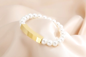 Macro shot of an elegant pearl bracelet with a polished gold metal bar on champagne silk