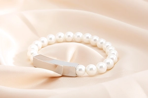 Close-up of pearl bracelet with a polished silver rectangular plate on soft silk