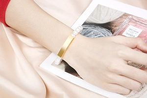 Close-up of pearl and gold square bar bracelet worn on wrist with elegant silk backdrop
