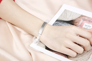 Detailed view of a pearl bracelet with a rectangular silver charm worn on the wrist