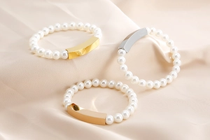 Detailed view of pearl bracelets in gold, silver, and rose gold on cream satin background