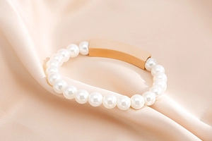 Macro detail of elegant pearl bracelet with a polished rose gold bar on silk fabric