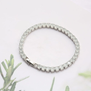 Detail view of silver tennis bracelet with round cut pale green gemstones and fold-over clasp
