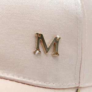 Macro shot of pink satin baseball cap featuring a premium gold metallic M logo detail