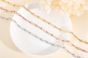 Detailansicht flacher S-Link Ketten in Gold, Roségold und Silber auf einer weißen Schale