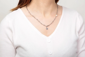 Detailaufnahme einer silbernen Stern-Halskette mit Perle am Hals eines Models