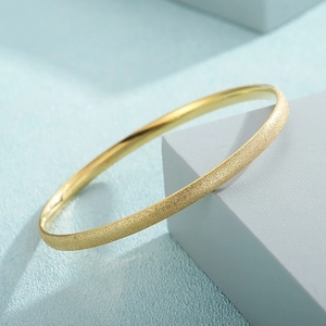Detail of minimalist gold-plated bangle with frosted exterior and polished inner surface