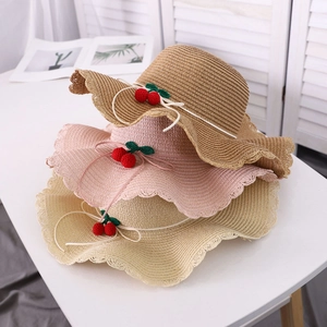 Detail of woven straw hats featuring wavy lace edges and red cherry pendants
