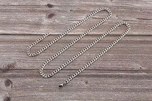 Detailed shot of silver Cuban link body chain with lobster clasp on a wooden background