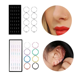 Multiple colorful stainless steel C-shaped nose rings and earrings shown in display boxes