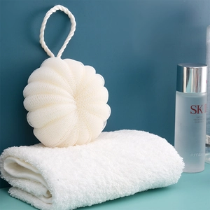 Close-up of a white mesh bath ball with a hanging rope placed on a soft towel