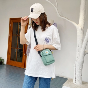 Close-up of light green canvas crossbody bag with white daisy embroidery and nylon strap