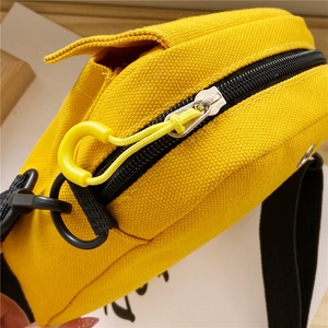 Detailed close-up of yellow canvas crossbody bag featuring zipper and strap attachment