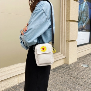 Street style view of a white canvas crossbody bag with sunflower embroidery and black strap