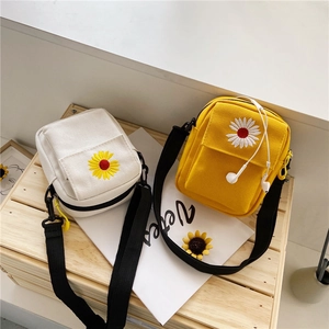 Detail of daisy embroidery on white and yellow canvas crossbody bags with shoulder straps