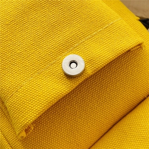 Detailed close-up of the silver magnetic clasp on a yellow canvas shoulder bag fabric