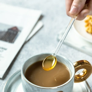 Cucchiaio in vetro resistente al calore con punta ambrata che versa sciroppo nel caffè
