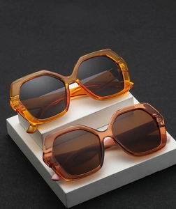 Detail of oversized geometric sunglasses in amber and brown on a minimalist pedestal