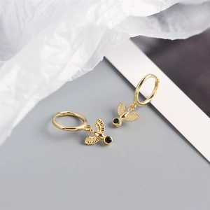 Detail of gold hoop earrings with bird pendant and black stone on aesthetic background