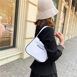 Detailed outdoor shot of a white nylon underarm bag with black piping and logo