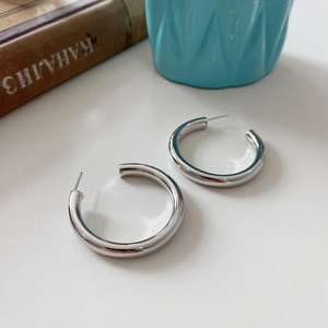 Detailed view of large silver C-shaped sterling silver hoop earrings on a white surface