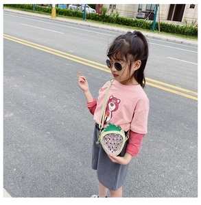 Detail of pink sequin strawberry crossbody bag worn by a child in an outdoor street setting