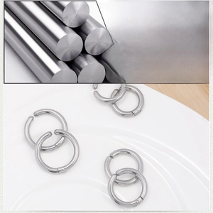 Polished silver titanium steel hoop earrings on white ceramic plate with metal raw material