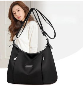 Close-up of black nylon shoulder bag with adjustable strap and silver logo plate detail