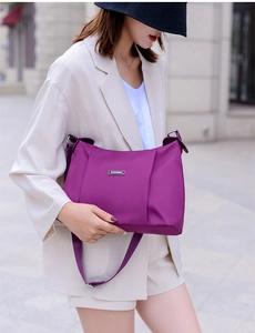 Close-up of a purple nylon crossbody bag worn by a model in a beige suit on a city street