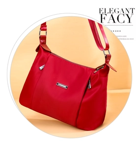 Detail view of red nylon crossbody bag showing the metallic logo and fabric shoulder strap