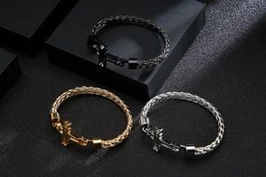 Detailed view of woven metal bracelets in black, gold, and silver with cross clasp design