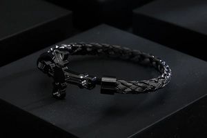 Detail of black woven metal bracelet featuring a bear-shaped buckle on dark background