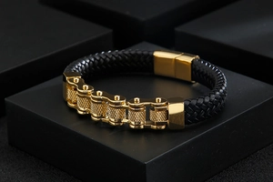 Detail of men's black braided leather bracelet with golden motorcycle chain on a stand
