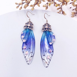 Macro detail of gradient blue and purple butterfly wing earrings with sparkling rhinestones