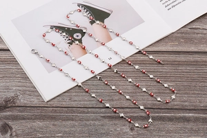 Détail d'un collier chaîne argentée avec perles œil rouge et pendentifs cœur polis
