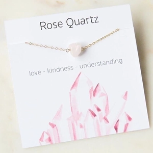 Detailed close-up of rose quartz stone on gold chain with card featuring love and kindness