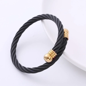 Detalle de pulsera de cable negro trenzado con terminales metálicos dorados sobre plato blanco