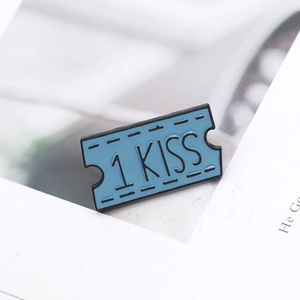 Blue ticket-shaped metal brooch badge with 1 KISS engraving on white paper background