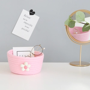 Pink hand-woven cotton rope storage basket with white flower accent on a white desk